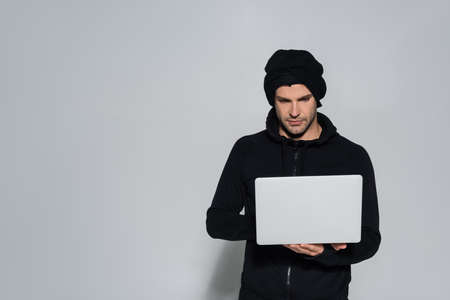 Hacker in balaclava using laptop on gray backgroundの写真素材