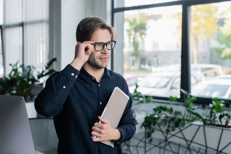 Programmer holding eyeglasses and paper folder near computer in office