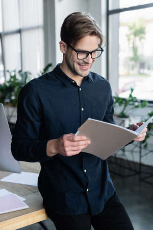 Young programmer looking at paper folder near computer in officeの写真素材