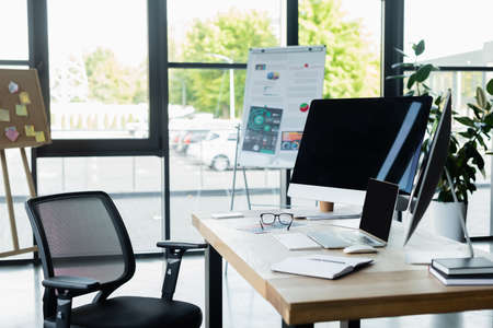 Computers with blank screen near notebook and eyeglasses on table in office