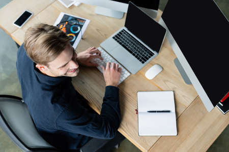 Overhead view of smiling developer using computers near smartphone and notebook on tableの写真素材