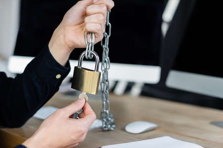 Cropped view of programmer holding padlock and key near blurred computers in officeの写真素材