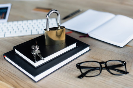 Padlock and keys on notebooks near eyeglasses and keyboard in officeの写真素材