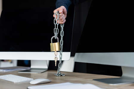 Cropped view of programmer holding padlock on chain near computers in office