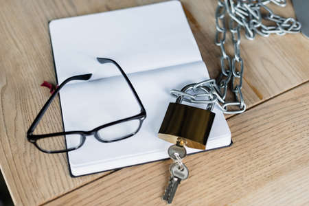 Eyeglasses near padlock and notebook on table in office