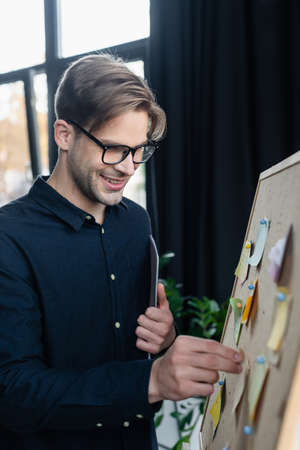 Positive developer with paper folder looking at sticky notes on board