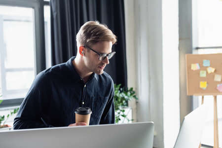 Young programmer in earphone holding coffee near computer monitorsの写真素材