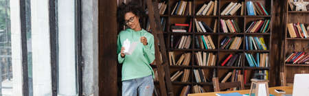 young african american woman in eyeglasses holding chopsticks near carton box with takeaway food,...