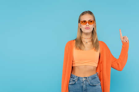 Pensive blonde woman in sunglasses having idea isolated on blue