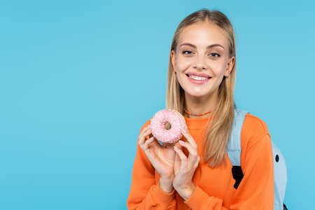 Positive student with backpack holding donut isolated on blueの写真素材