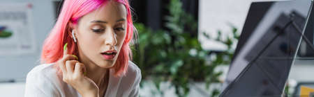 pierced businesswoman with pink hair in earphone looking away, bannerの写真素材