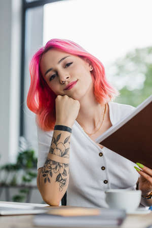 smiling businesswoman with pink hair holding folder in officeの写真素材