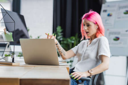 laptop near blurred businesswoman with pink hair gesturing in officeの写真素材