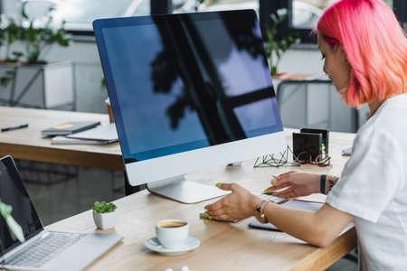 pierced businesswoman with pink hair looking at computer keyboardの写真素材