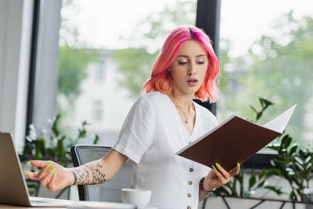 displeased businesswoman with pink hair holding folder in office