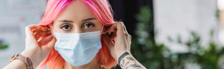 tattooed young manager with pink hair wearing medical mask in office, bannerの写真素材