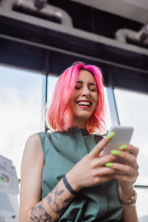 low angle view of smiling businesswoman with pink hair using smartphoneの写真素材