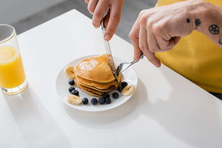 Cropped view of man cutting pancakes near berries and banana at homeの写真素材