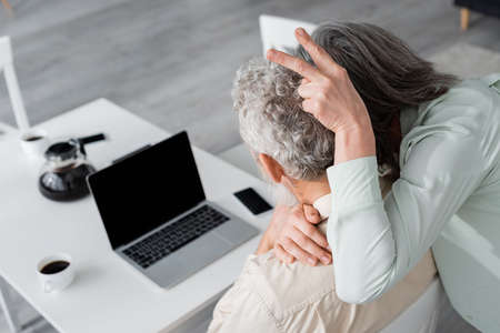 Mature woman showing peace gesture near husband and blurred devices at home