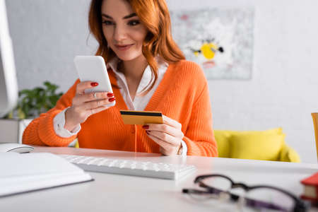blurred woman smiling while holding credit card near keyboard at homeの写真素材