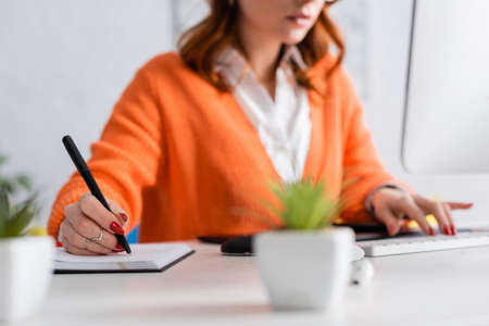 cropped view of blurred woman writing in notebook and typing on keyboard at homeの写真素材