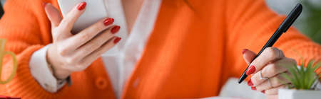 cropped view of blurred woman with pen using smartphone at home, banner