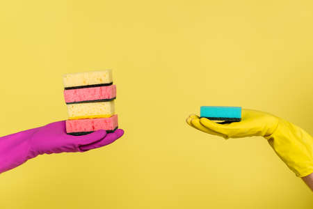 partial view of woman and man in rubber gloves holding sponges isolated on yellowの写真素材