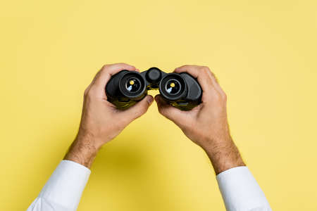 cropped view of man holding black binoculars in hands on yellowの写真素材