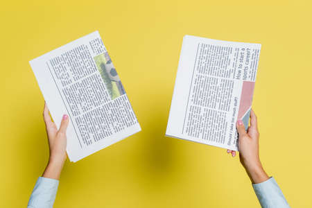 cropped view of woman holding newspapers on yellow