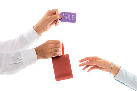cropped view of man holding shopping bag and price tag near female hand isolated on whiteの写真素材