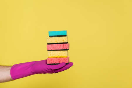 partial view of man in rubber glove holding stack of sponges isolated on yellow