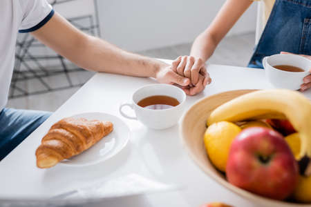 cropped view of couple holding hands during breakfast