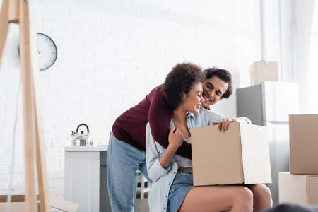 happy interracial couple hugging near carton boxes