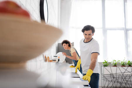 young man cleaning kitchen cabinet with rag near curly african american woman in kitchenの写真素材