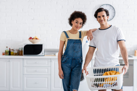 happy interracial couple near basket with dirty laundryの写真素材