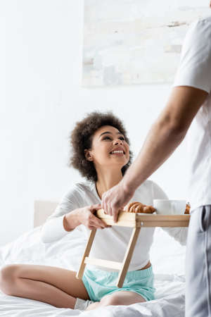 joyful african american woman taking breakfast tray near boyfriendの写真素材