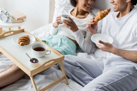cropped view of cheerful interracial couple having breakfast in bedの写真素材