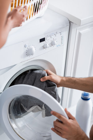 cropped view of man holding laundry near washing machine and blurred african american girlfriendの写真素材