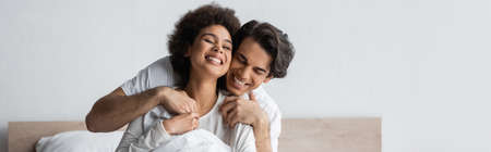 cheerful man hugging pleased african american woman, banner