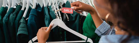 cropped view of african american saleswoman holding hanger with sale tag in clothing boutique, bannerの写真素材