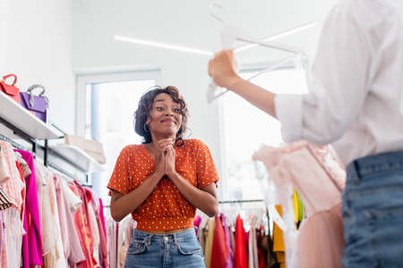 joyful african american woman looking at friend holding pink dress on hangerの写真素材
