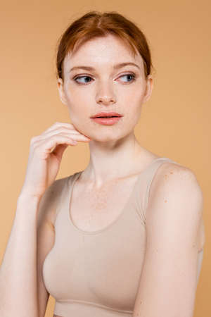 Freckled woman in top touching face isolated on beigeの写真素材