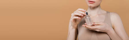 Cropped view of young woman holding bottle with cosmetic serum isolated on beige, bannerの写真素材