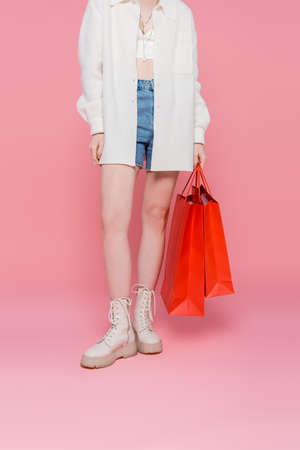 Cropped view of young stylish woman holding shopping bags on pink backgroundの写真素材