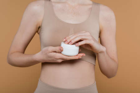 Cropped view of woman in top holding container with cream isolated on beigeの写真素材
