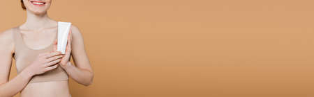 Cropped view of positive freckled woman holding tube with lotion isolated on beige, bannerの写真素材
