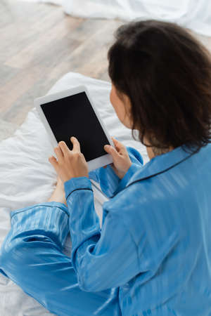 high angle view of blurred young woman in blue pajamas using digital tablet with blank screenの写真素材