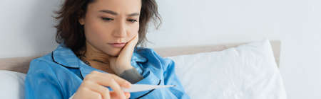 sick young woman looking at electronic thermometer, banner