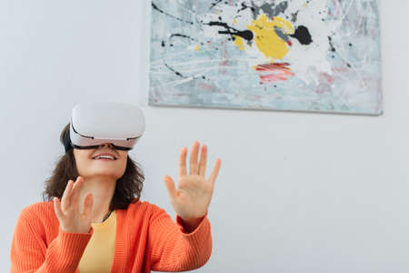 young happy woman in vr headset gesturing during simulation game at homeの写真素材