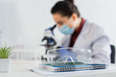 goggles on notebook near blurred scientist near microscopeの写真素材